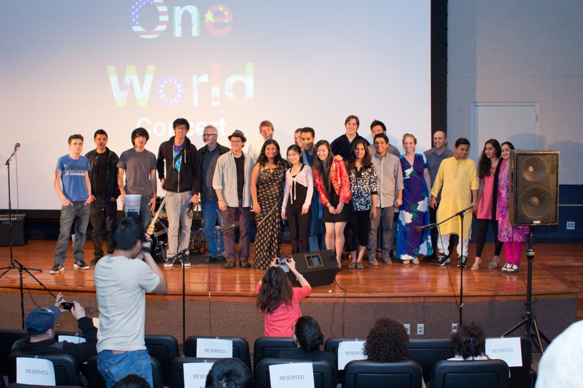 a group of students in various international clothing on a stage with the words "One World Concert" behind them